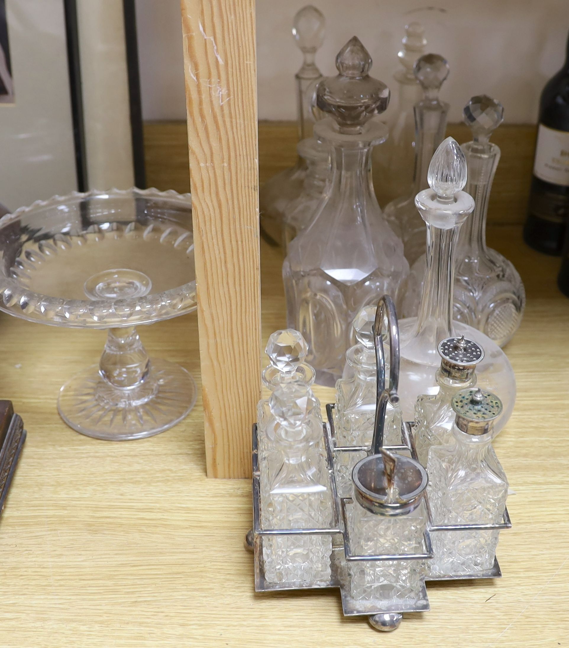 Sundry glassware including a six bottle cruet set on a plated stand, a Victorian cut glass jug, a pair of long neck decanters, five other decanters and a glass cake tazza